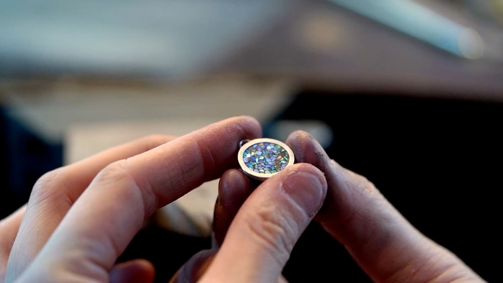 A finished pendant with a mother-of-pearl mosaic inlay held between fingers
